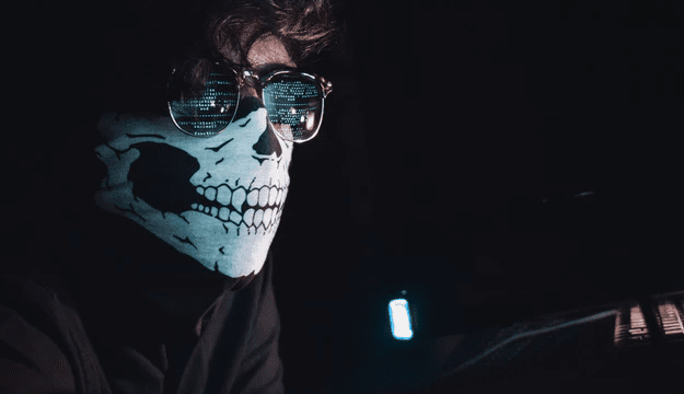 Hacker com óculos escuros e bandana no rosto mexendo em computador