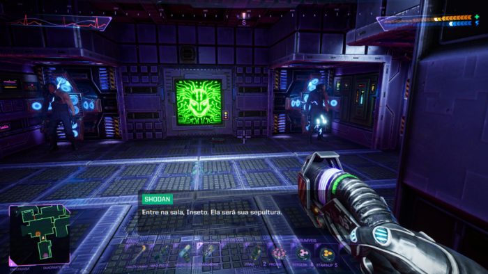 Uma visão em primeira pessoa do System Shock mostra um braço segurando uma arma futurística. Dois inimigos robóticos estão de cada lado, iluminados por luzes azuis, com uma tela verde no centro exibindo um rosto ameaçador. Os elementos do HUD do jogo ficam visíveis, incluindo uma mensagem
