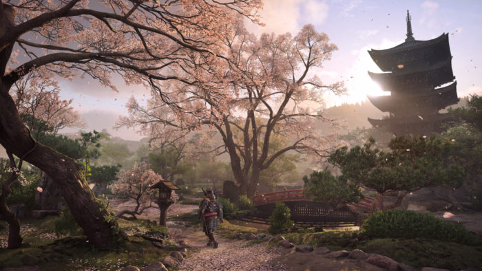 A imagem mostra uma bela paisagem de Assassins's Creed Shadows com árvores floridas e Yasuke caminhando entre elas